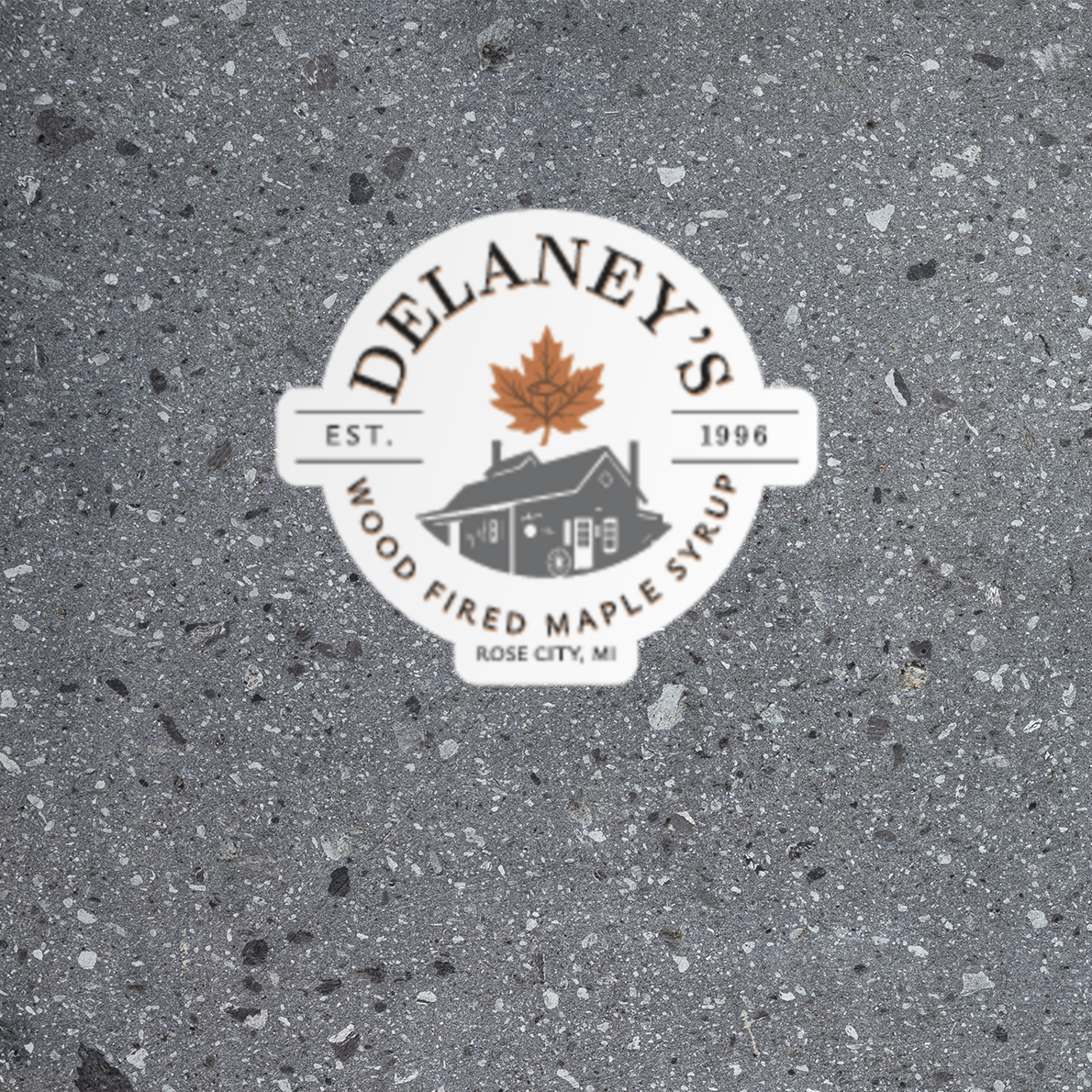 Delaney's Wood Fired Maple Syrup logo sticker on a gray concrete background